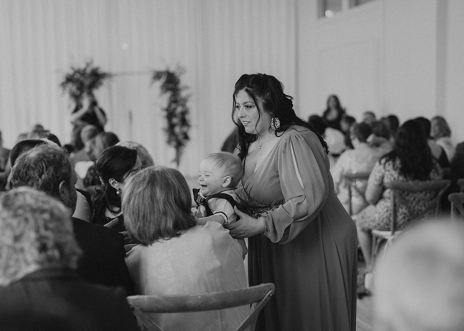 black and white image of wedding guest holding her baby and talking to other people