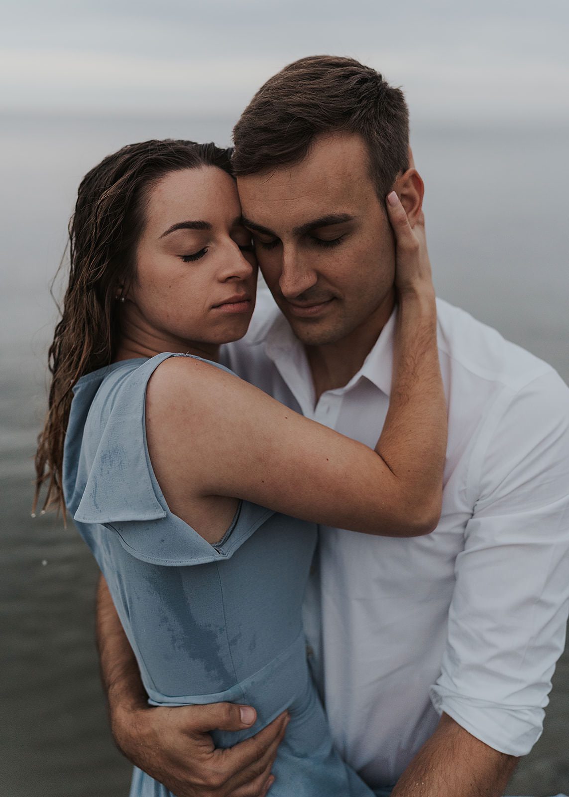 engaged couple with heads together and eyes closed while standing in a lake