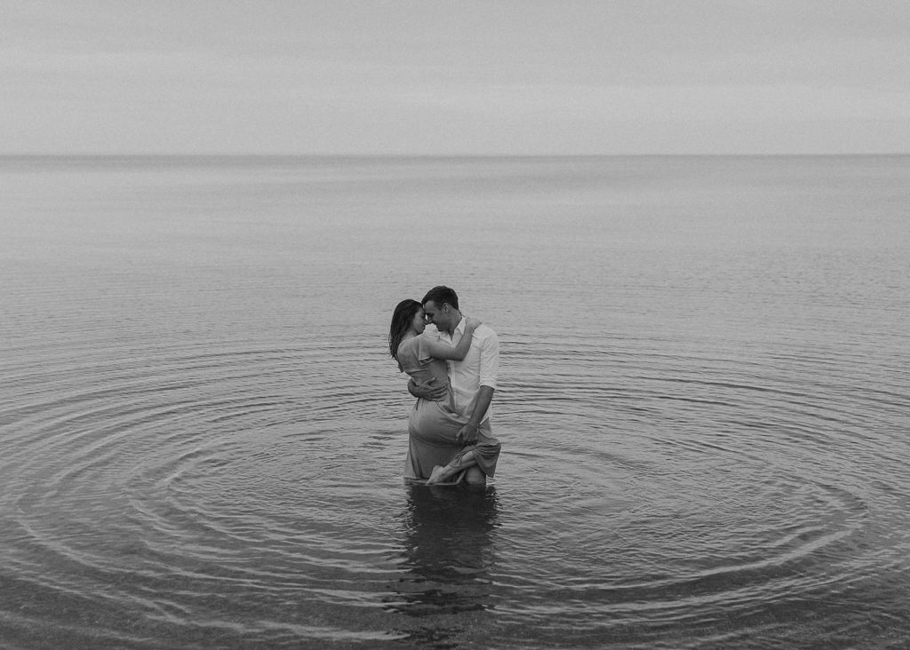 engaged couple in the water in formal attire while doing a sensual embrace during their engagement session