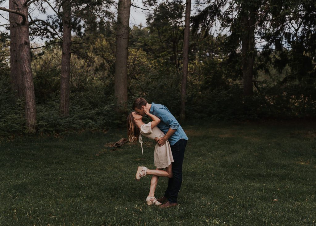 Fiance dipping his girlfriend back while kissing her in the forest