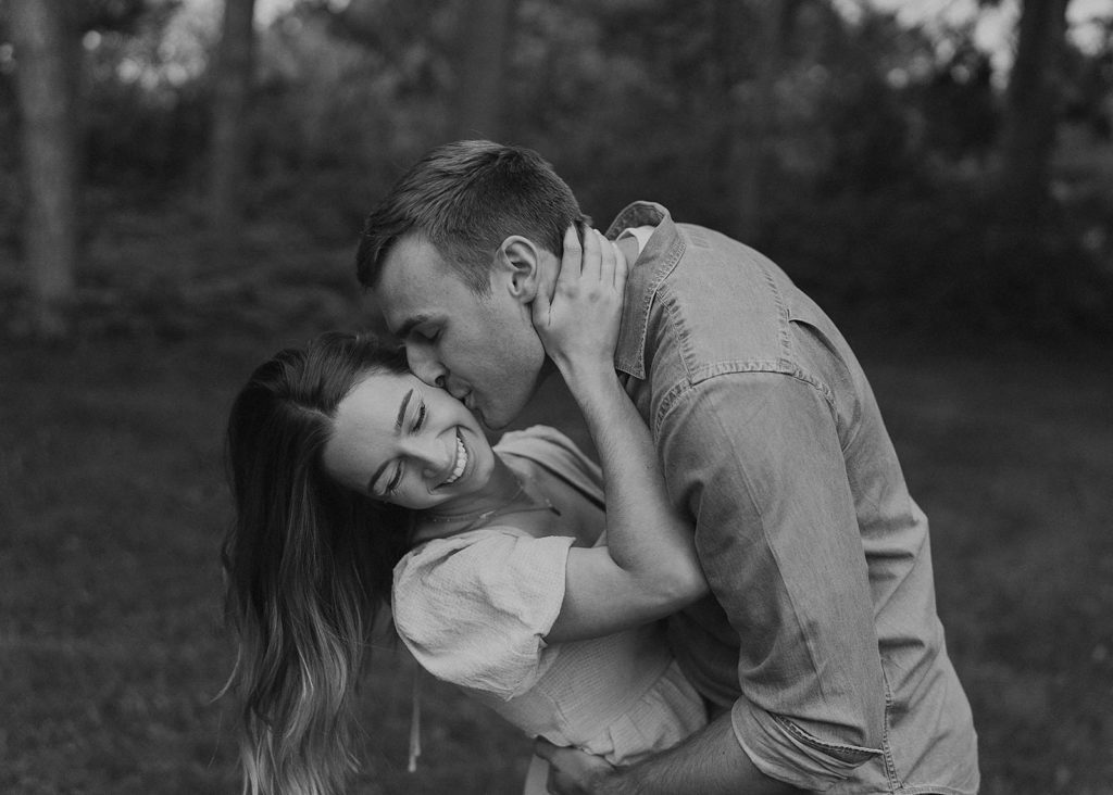 black and white image of boyfriend kissing his fiancees cheek while dipping her