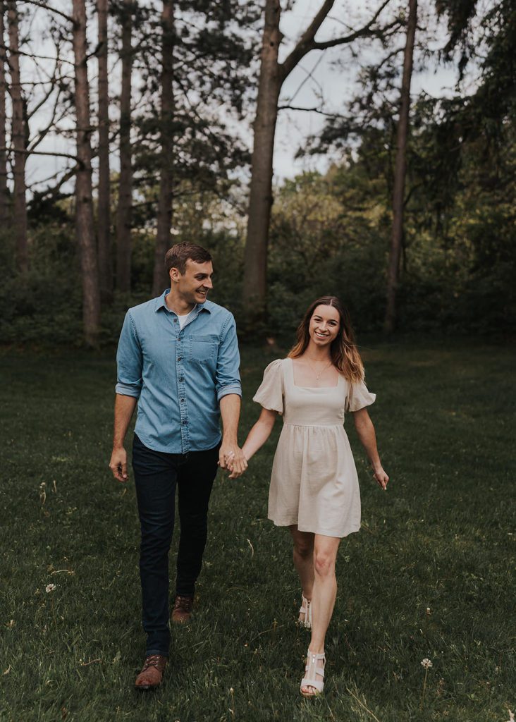 engaged couple holding hands walking through the forest during their engagement session