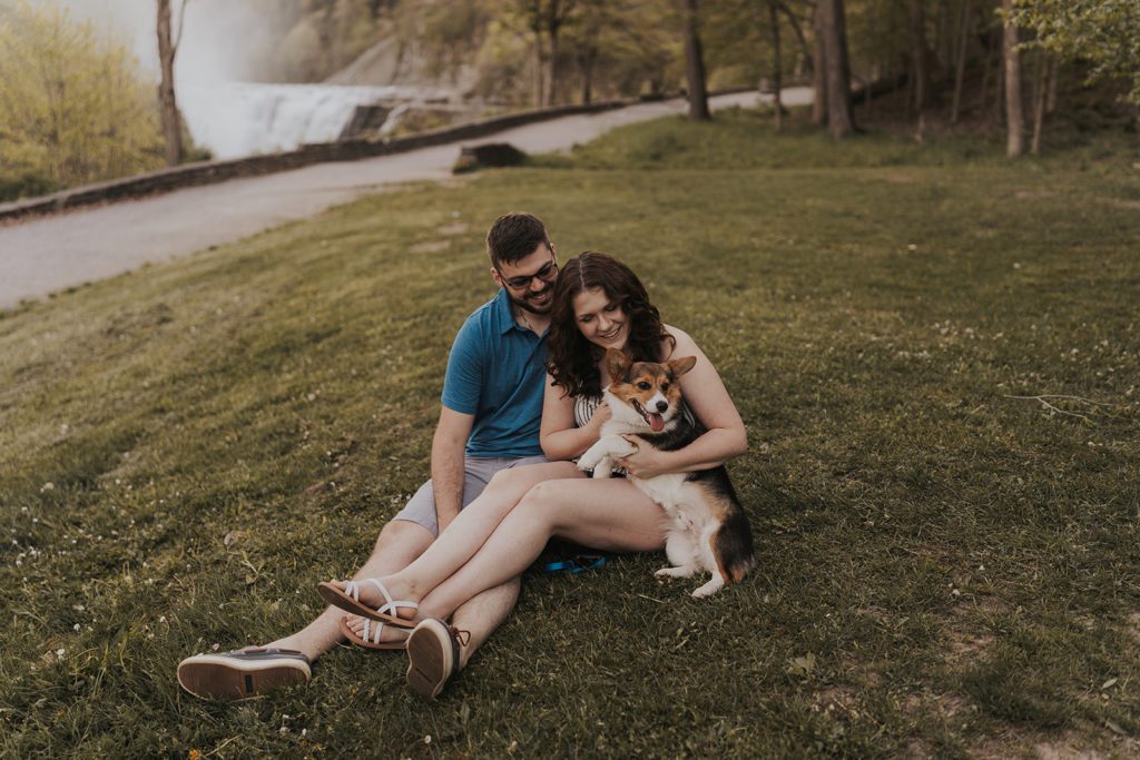 pet parents sitting on the grass with their corgi in their laps during their furry friend engagement session