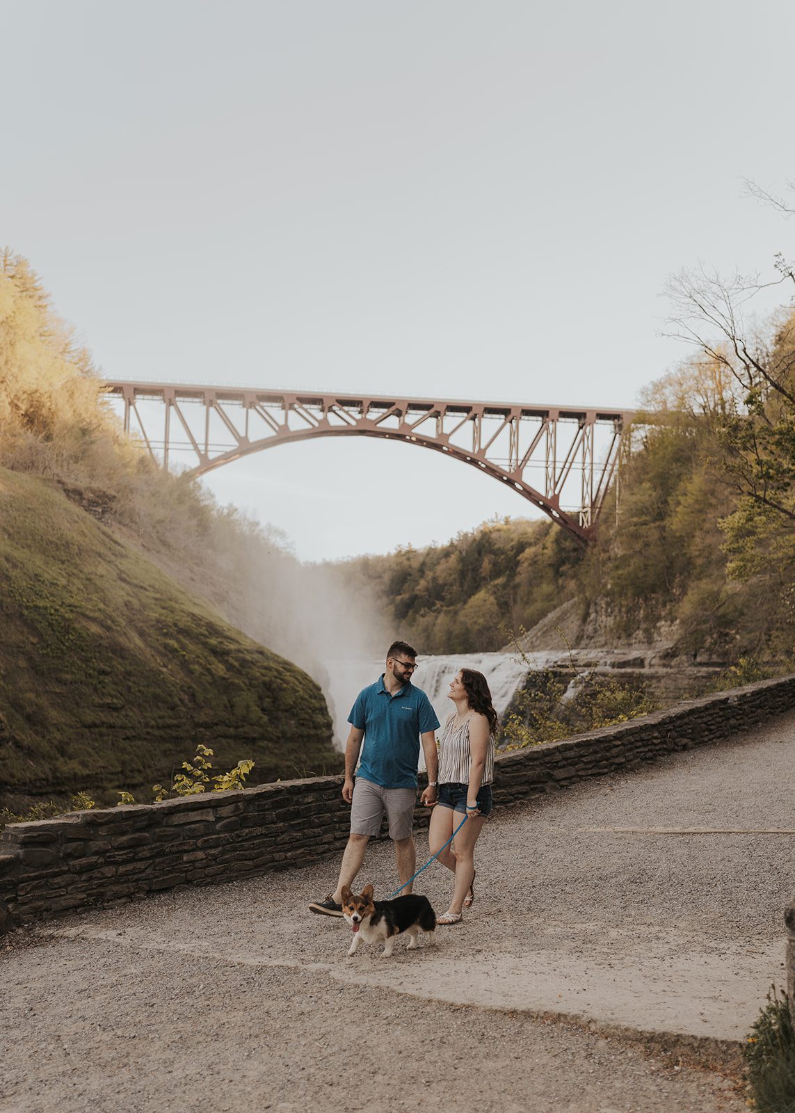 couple walking around with their corgi in front of a waterfall in upstate new york