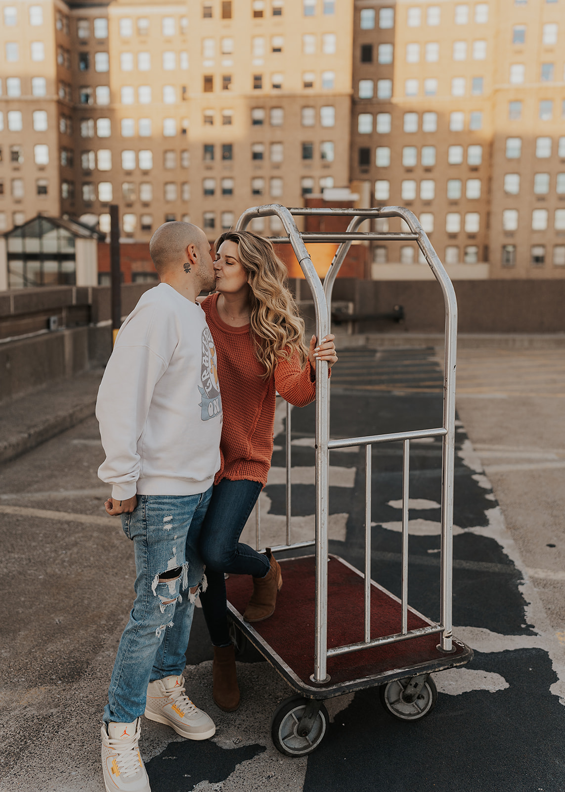couple kissing on a bell-hop cart on top of a parking garage in downtown rochester during their engagement session