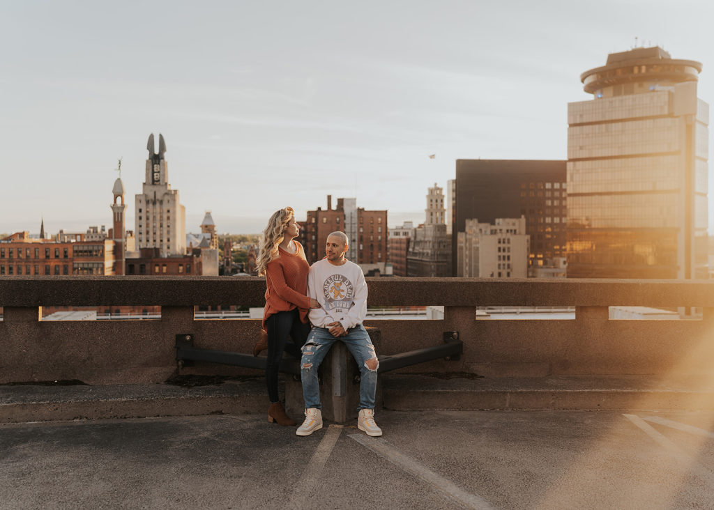 couple sitting on top of a parking garage in rochester ny during their engagement session