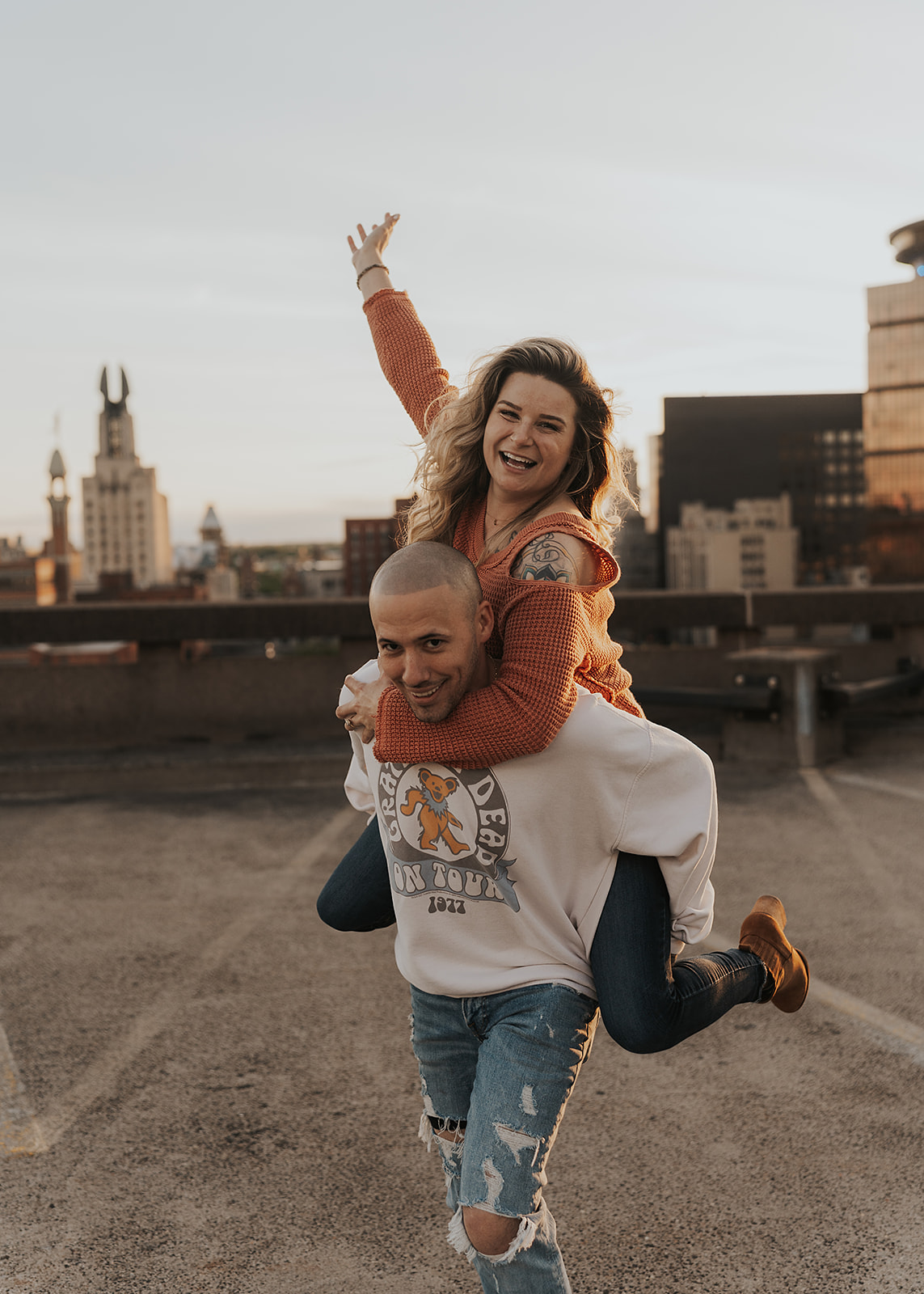 fiance giving his girlfriend a piggy back ride wile on top of a parking garage during their engagement session