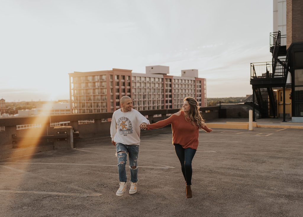 couple running on top a parking garage in downtown rochester during their engagement session