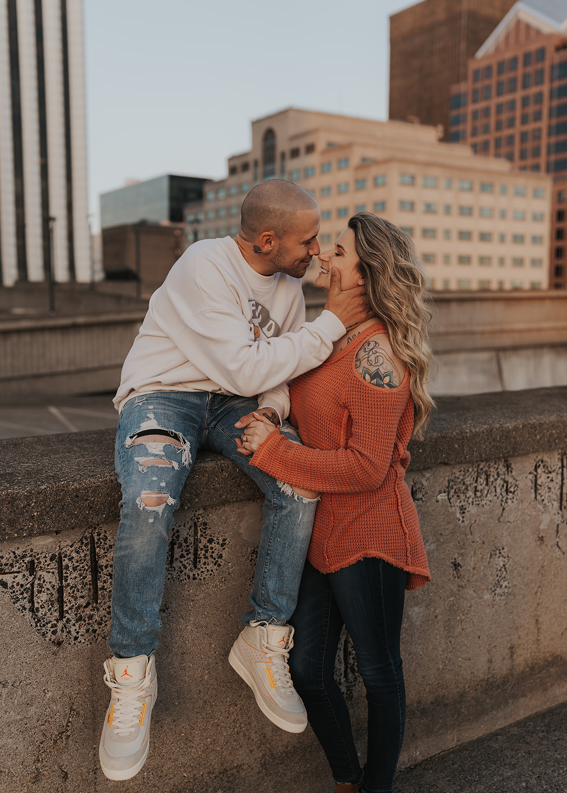fiancé holding his girlfriends face while seated on the edge of a parking garage roof in the city of rochester during their engagement session