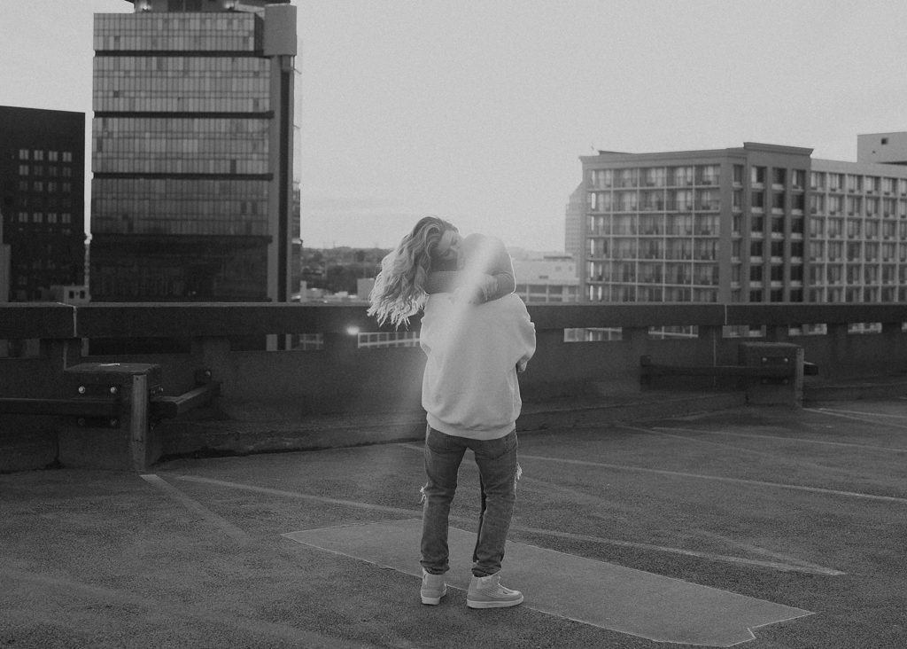 black and white photo of boyfriend picking his girl friend up on top of a parking garage