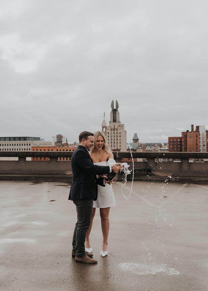engaged couple popping champagne on the rooftop of a parking garage in Rochester NY