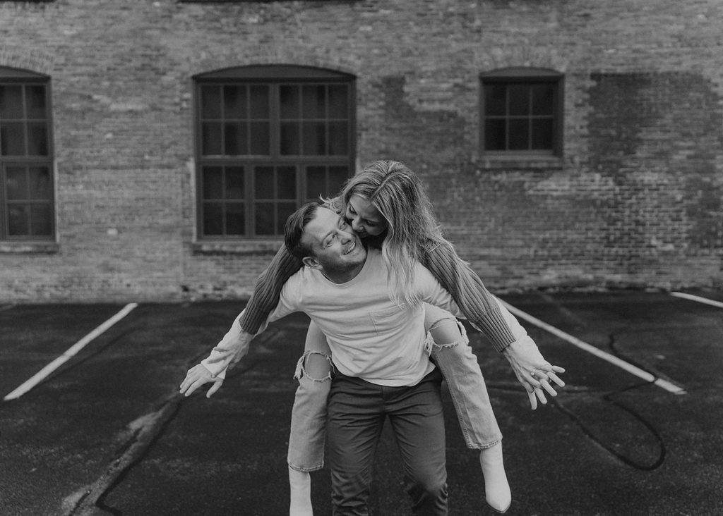 Fiance giving his girlfriend a piggyback riding during their engagement photos in Rochester NY