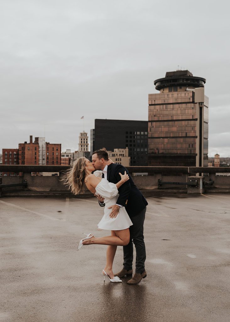 Fiance kissing his girlfriend on the rooftop of a parking garage in Rochester NY