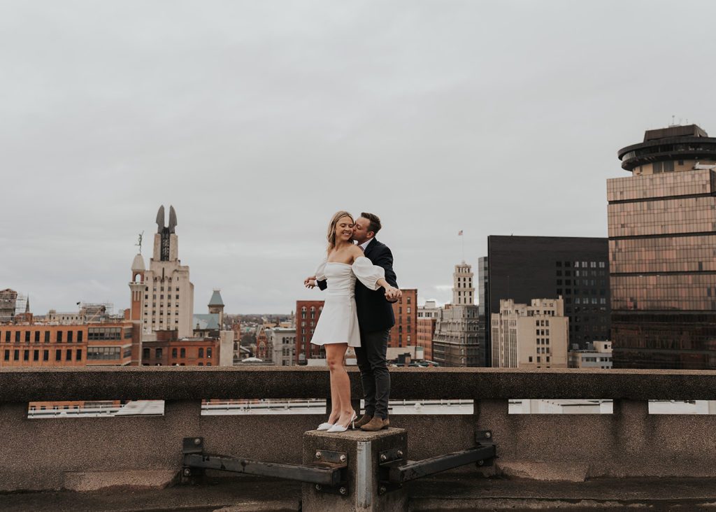 engaged couples standing on the roof top of a parking garage in Rochester NY during their engagement photos