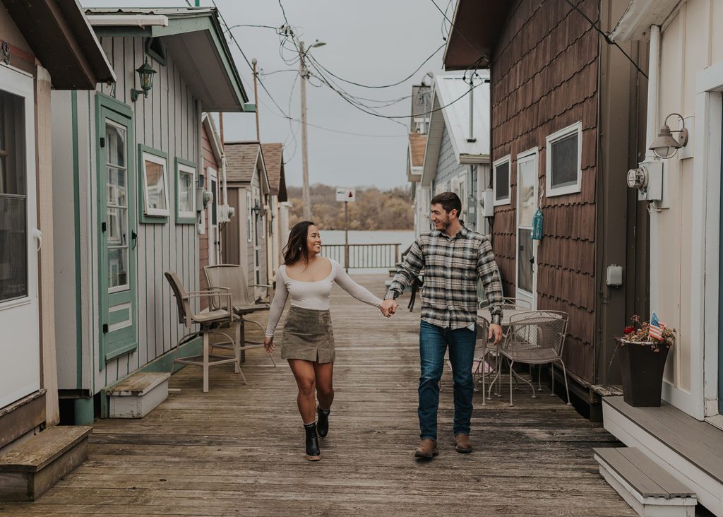engaged couple holding hands and walking down the pier during their engagement photos in Rochester NY
