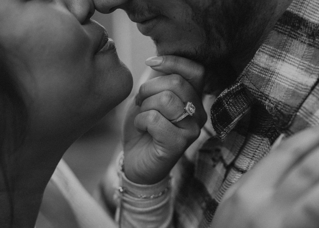 black and white image of cassie holding brandons chin featuring her engagement ring as the main focus of the photo