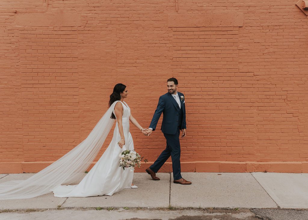 groom leading bride down the sidewalk during their wedding portraits in Rochester NY