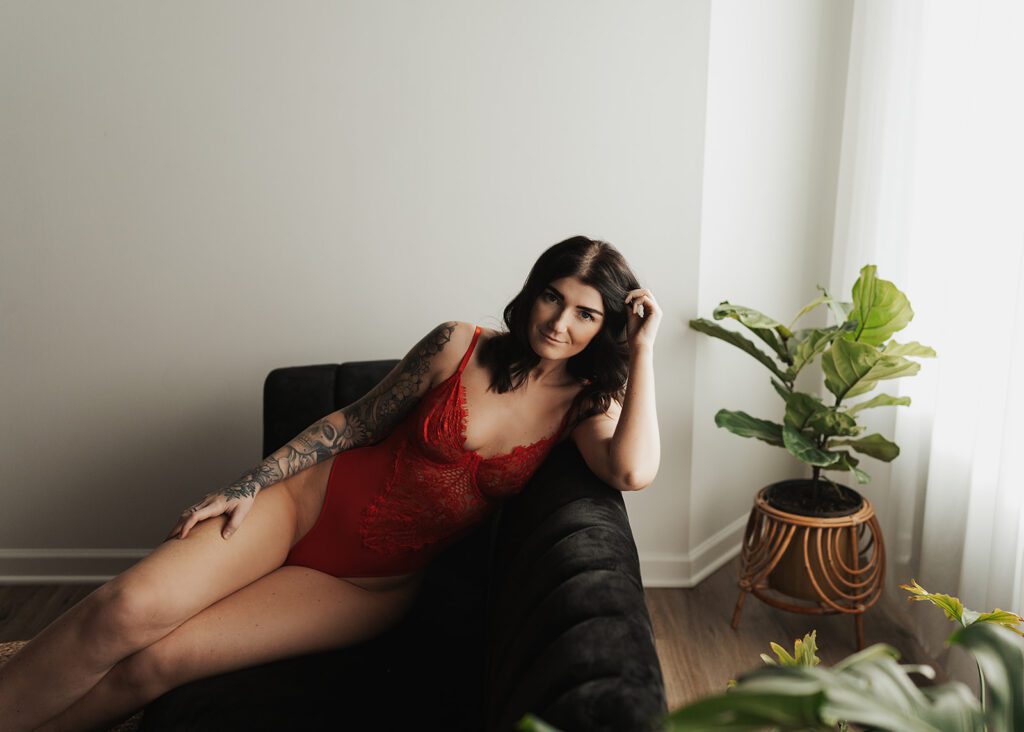 women wearing red lingerie sitting on a couch during her rochester ny boudoir photoshoot at gallery 48 photography studio