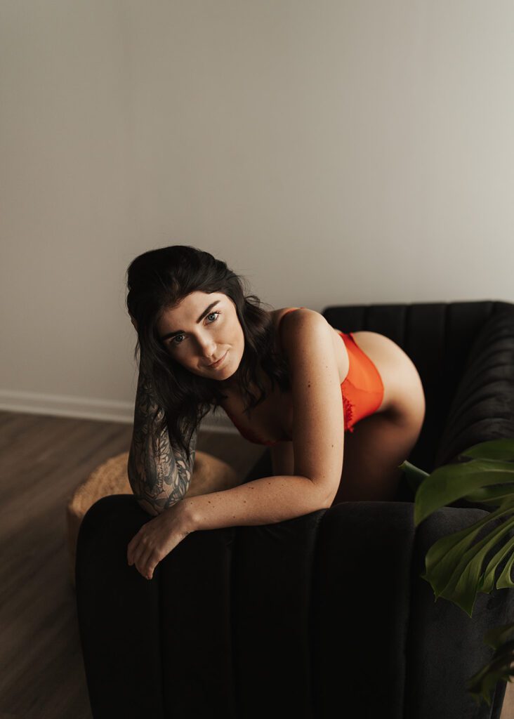 brunette tattooed women wearing red lingerie laying on a velvet green couch looking at the camera during her rochester ny boudoir photoshoot at gallery 48 photography studio