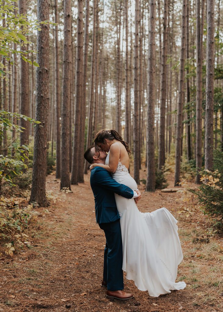 Groom picking up his bride and kissing her in the forest at Cummings Nature Center a Rochester NY Wedding Venue