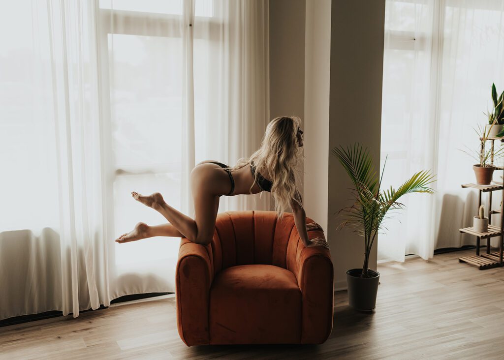 blonde women posed on top of an orange chair during her boudoir photoshoot at gallery 48 photography studio in Rochester NY