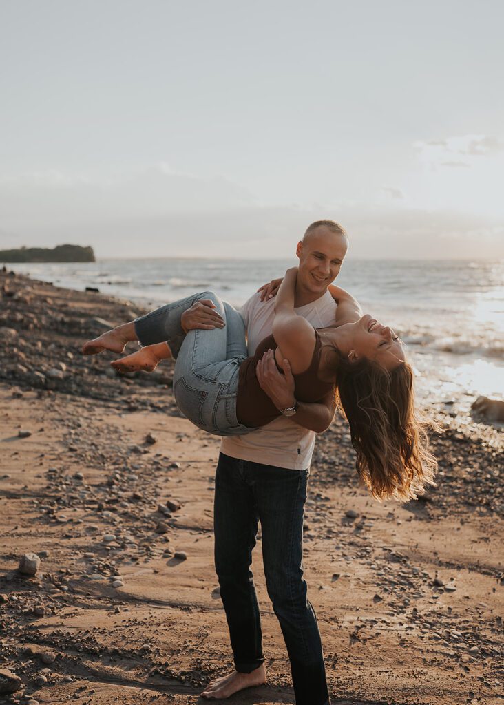 fiance picking up his girlfriend and swinging her around during their beach engagement photoshoot