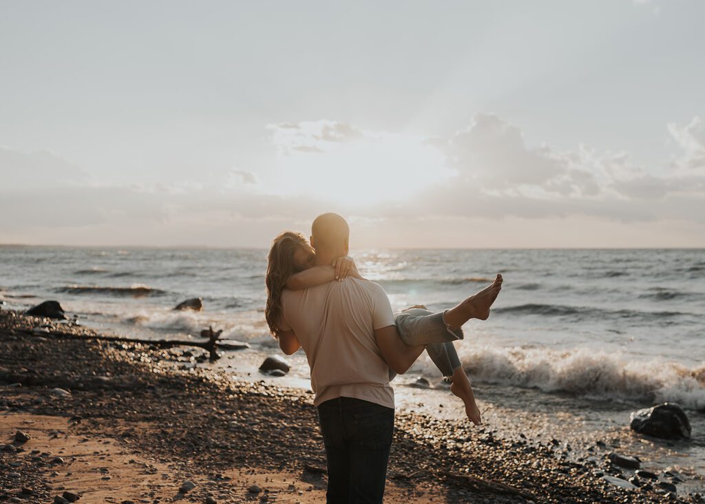 Fiance carrying his girlfriend on the beach during their engagement photoshoot