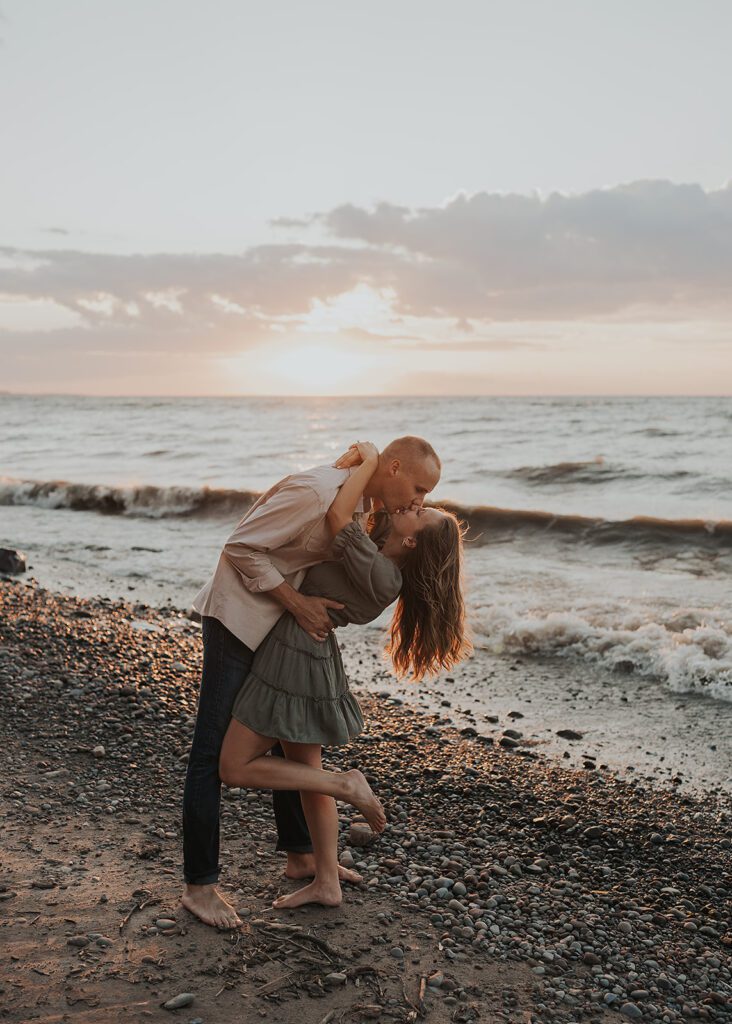 fiance dipping his girlfriend backwards as he kisses her during their beach engagement photoshoot
