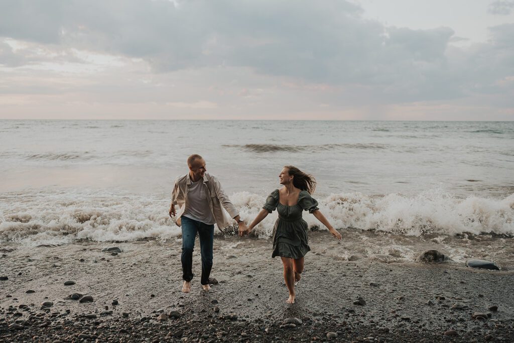 engaged couple running out of the water during their beach engagement photoshoot