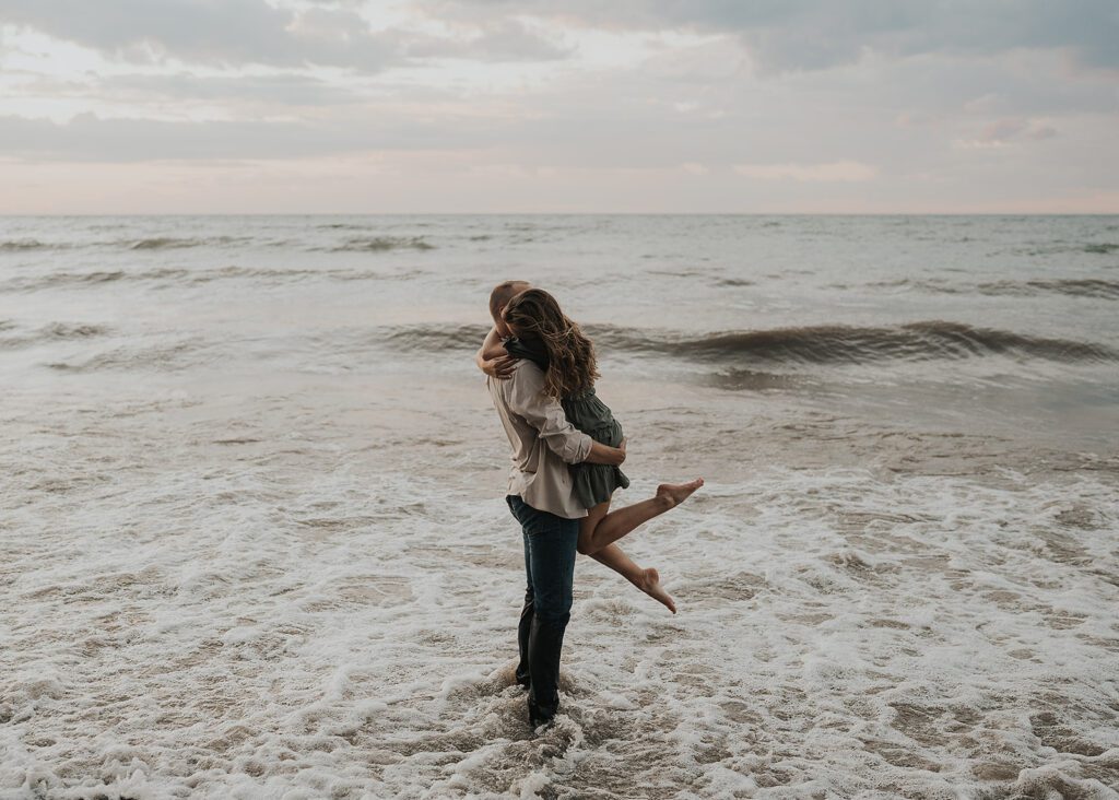 fiance picking his girlfriend up in the water at the beach during their beach engagement photoshoot