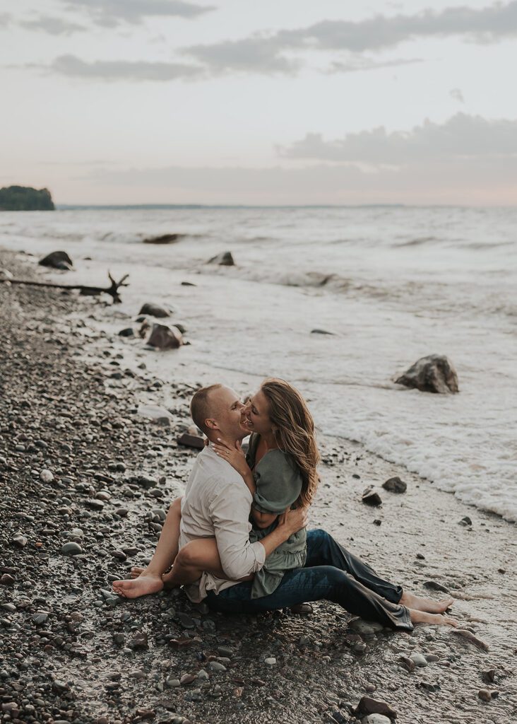 engaged couple sitting snuggled up on the beach in the water during their beach engagement session