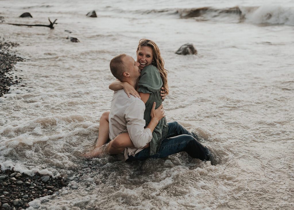 couples sitting in the water during their beach engagement photoshoot in rochester ny