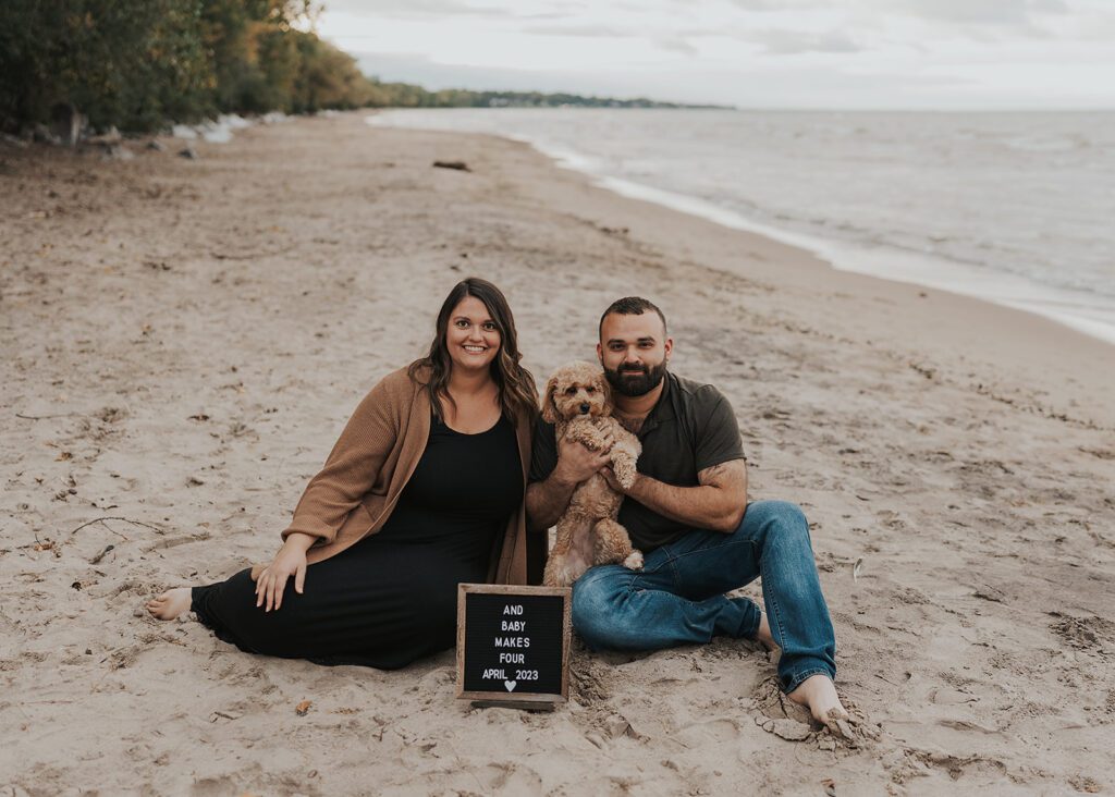 married couple sitting on the beach with their dog during their pregnancy announcement photoshoot