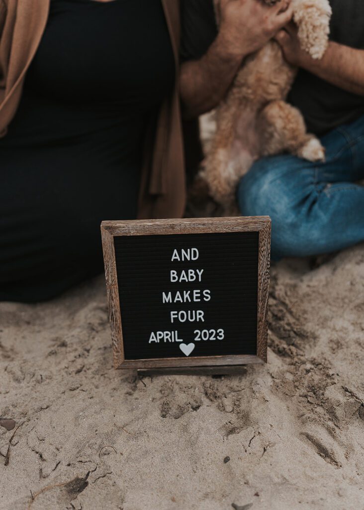 baby announcement sign sitting on the beach with couple in the background