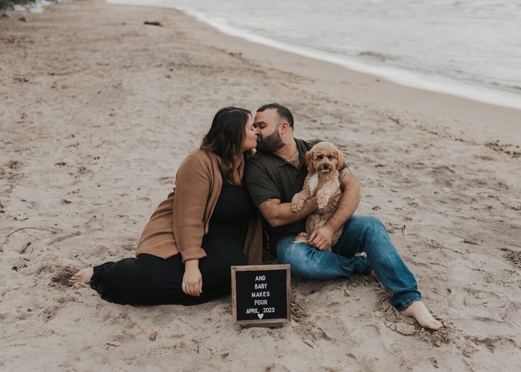 couple sitting on the beach in rochester ny during their pregnancy announcement photoshoot