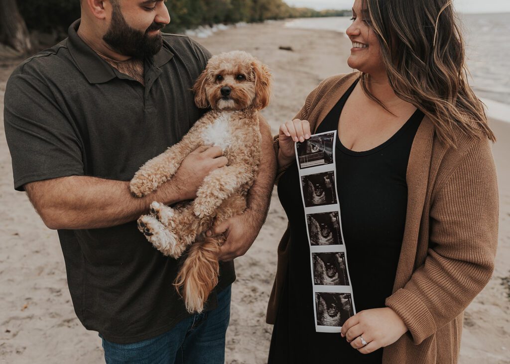 dog being held by his dad while wife is holding a baby sonogram during their pregnancy announcement photoshoot