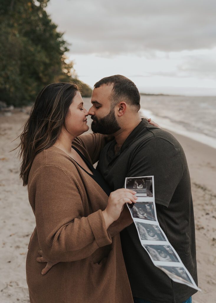 married couple smiling and looking at eachother as the wife holds a baby sonogram in her hands during their pregnancy announcement photoshoot in rochester ny