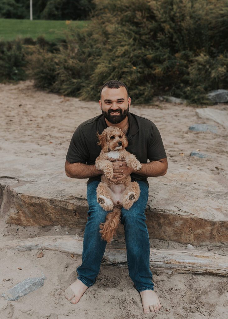 husband holding their pet dog on the beach during their pregnancy announcement photoshoot